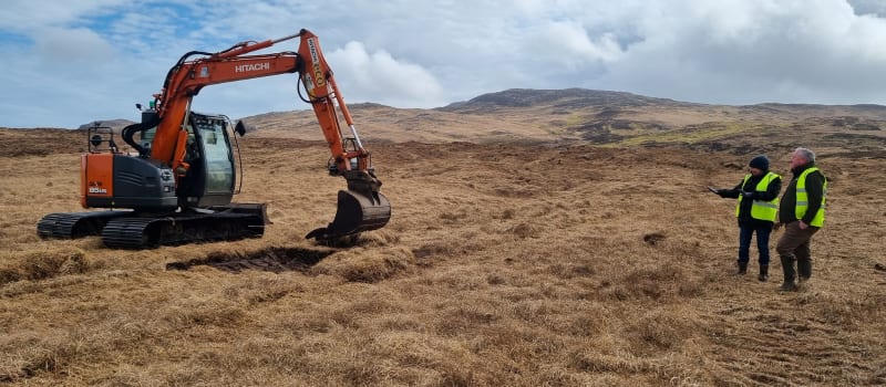 Digger creating a peat bank with two people watching